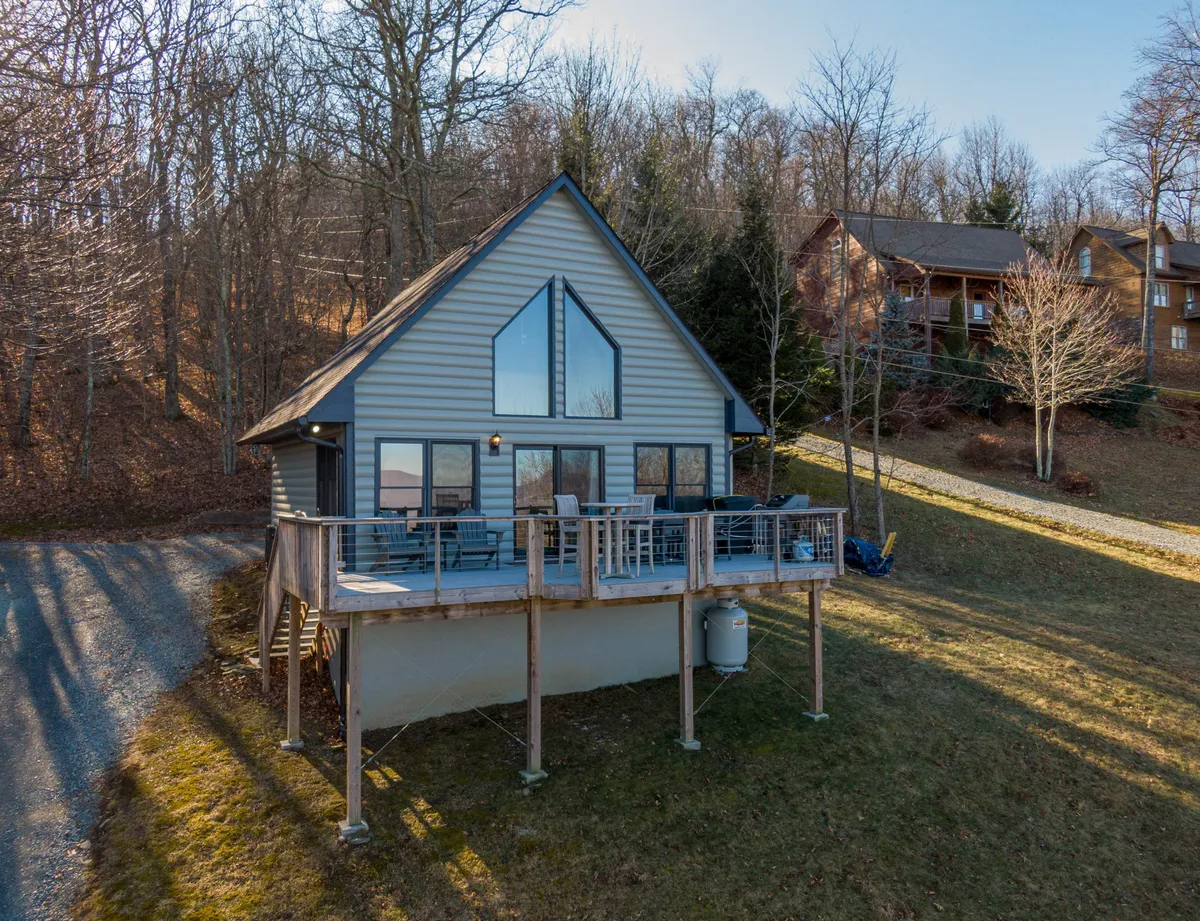 A modern cabin with large triangular windows and a spacious deck perched on a wooded mountainside, offering sweeping long-range views. The deck invites relaxation, perfect for morning coffee or evening stargazing, framed by the natural beauty of Boone, NC.