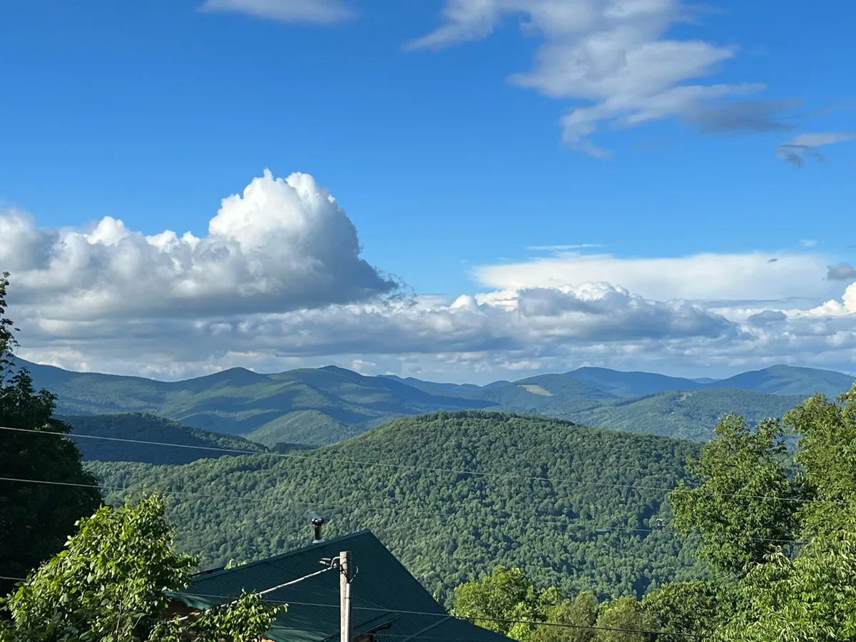 A wide, captivating view of a lush mountain range under a sky dotted with clouds. The untouched greenery and vastness invite exploration and outdoor activity, highlighting the scenic landscape surrounding Owen’s Perch.