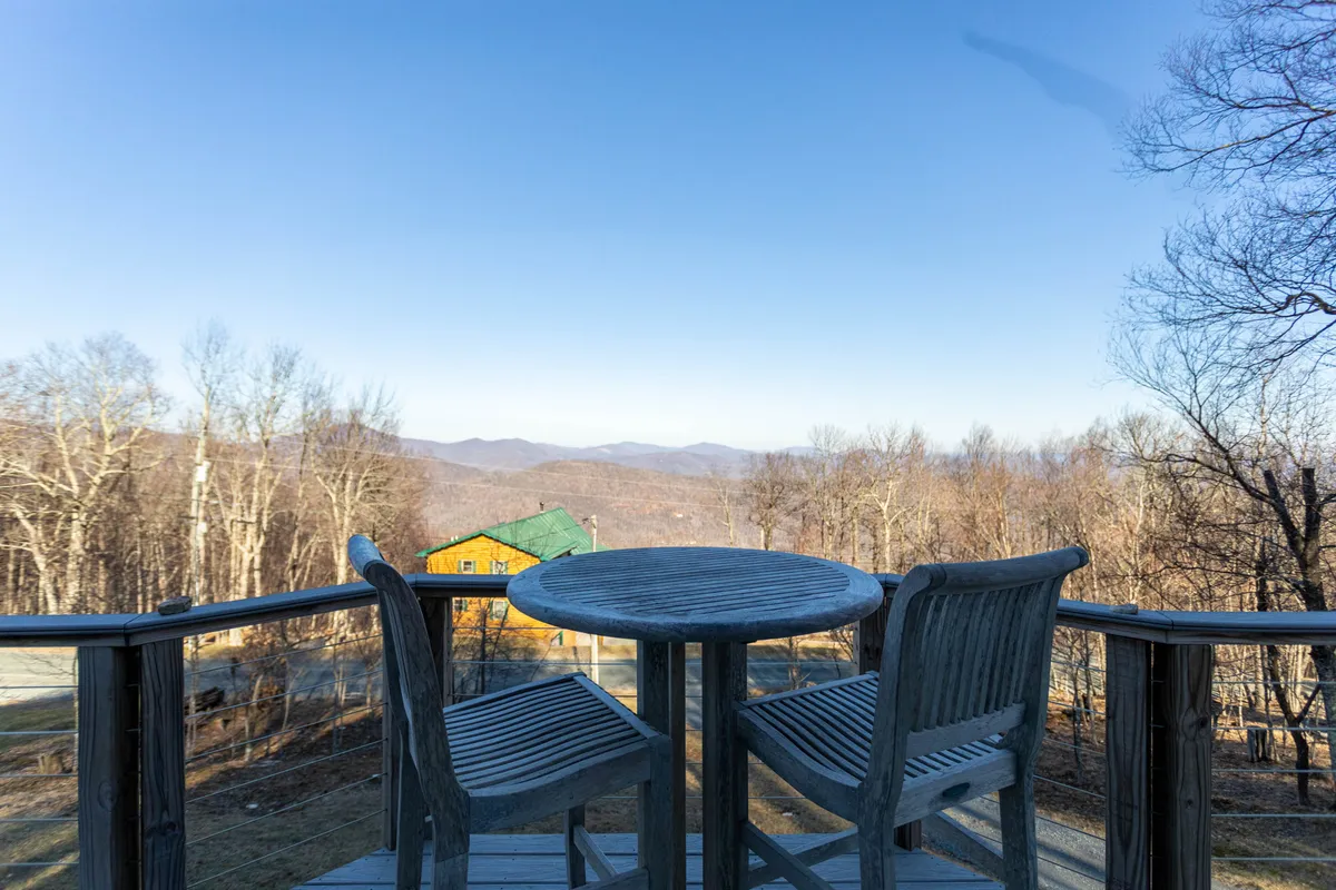 A wooden table with two chairs positioned to face a panoramic mountain view, set on a private deck. The tranquil setting is perfect for enjoying morning coffee, reading, or taking in the stars after a day of adventure.